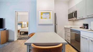 A modern hotel room with a dining area, kitchenette, and a bed with a view.