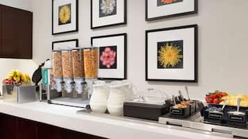 Ein Frühstücksbuffet mit verschiedenen Speisen, darunter Waffeln, Granola, Milch, Joghurt und Obst.