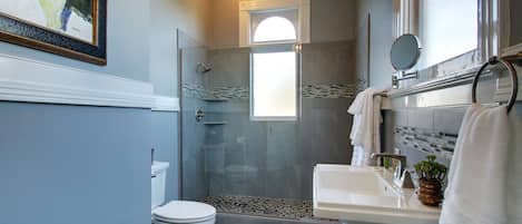A modern bathroom with a glass-enclosed shower, a white toilet, and a sink with a mirror.
