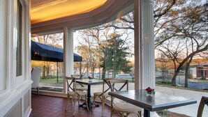 A covered patio with a table and chairs, a view of the street and trees, and a blue umbrella. - Hotel Finial, BW Premier Collection (Anniston)