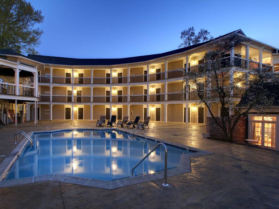 Um hotel com vários andares, piscina e área externa com mesas e cadeiras.