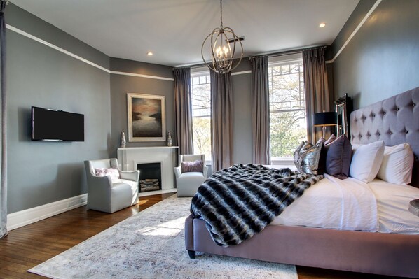 Une chambre moderne avec un grand lit, une cheminée, un téléviseur et un lustre.
