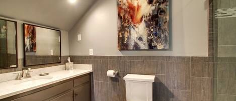 A modern bathroom with a large mirror, a white toilet, and a painting on the wall.
