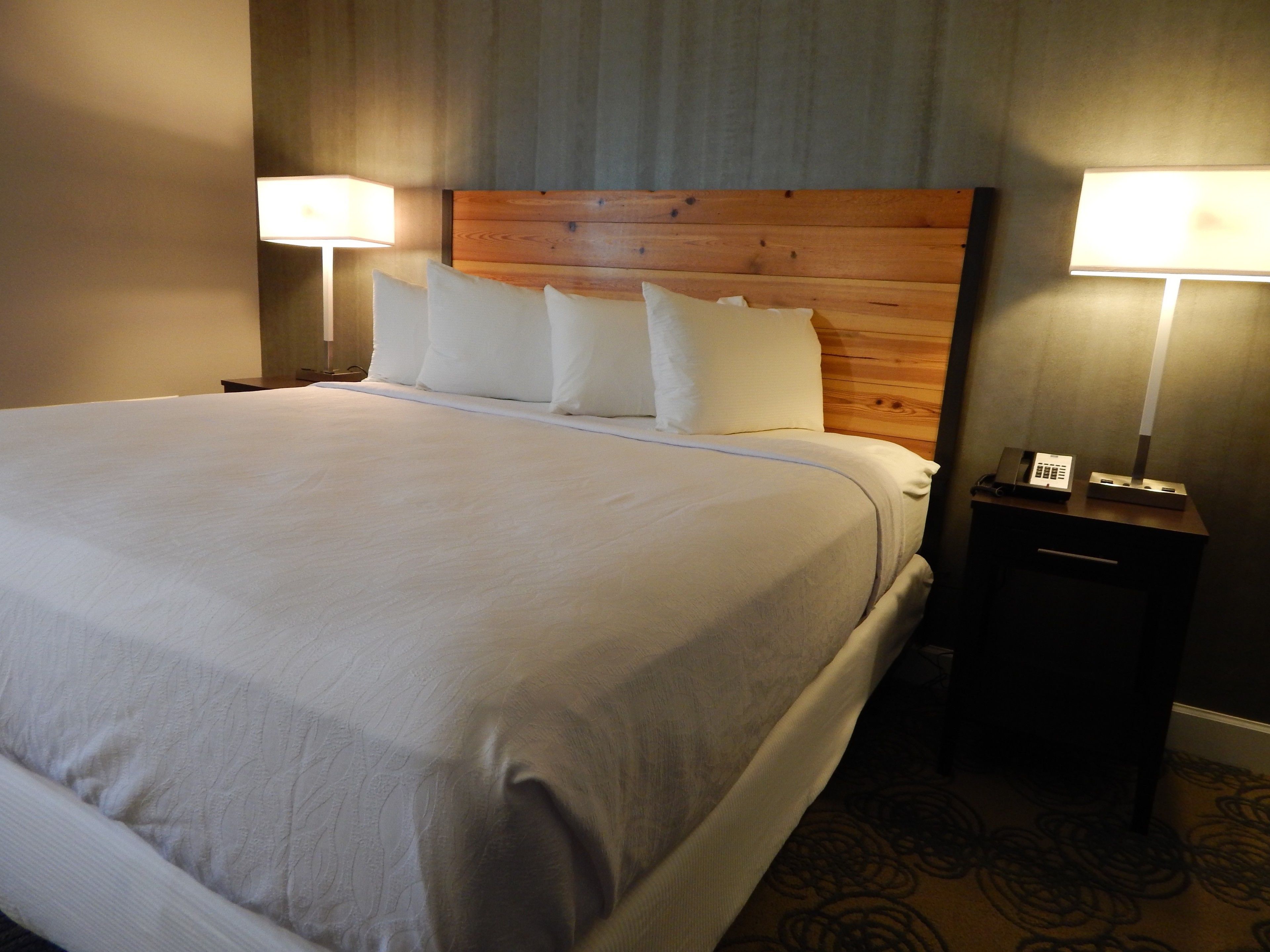 Una cama bien hecha con sábanas blancas, cabecera de madera y dos lámparas de noche.