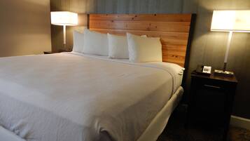 Una cama bien hecha con sábanas blancas, cabecera de madera y dos lámparas de noche.