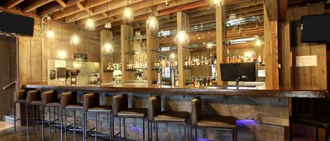 Zona de bar con vigas de madera, lámparas colgantes y taburetes.