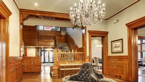 A spacious living area with a grand staircase, a chandelier, and a plush ottoman. - Hotel Finial, BW Premier Collection (Anniston)