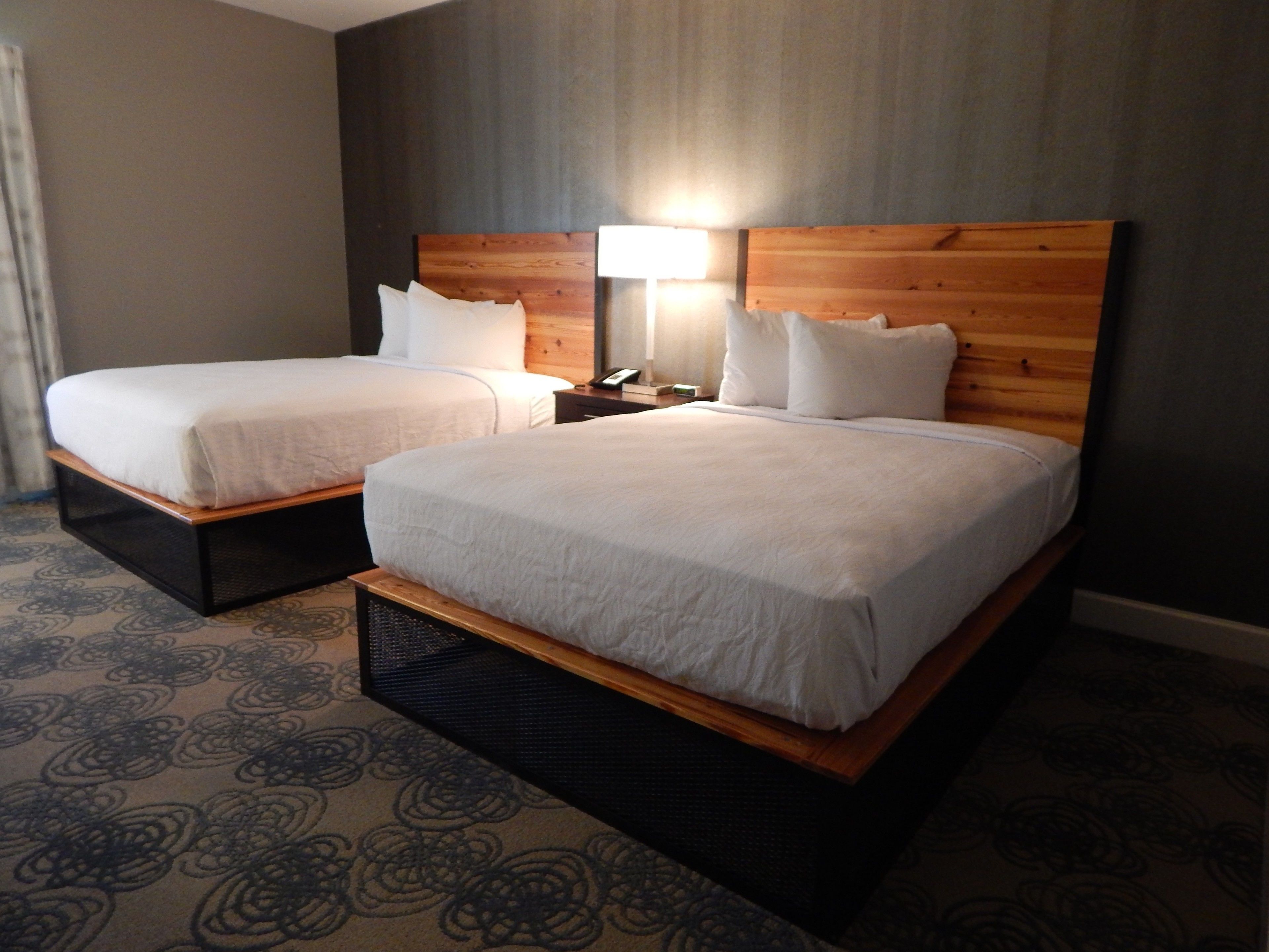 A hotel room with two beds, a nightstand, and a lamp.