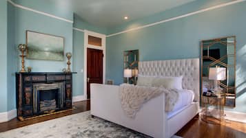 A bedroom with a white bed, a fireplace, and a large mirror.