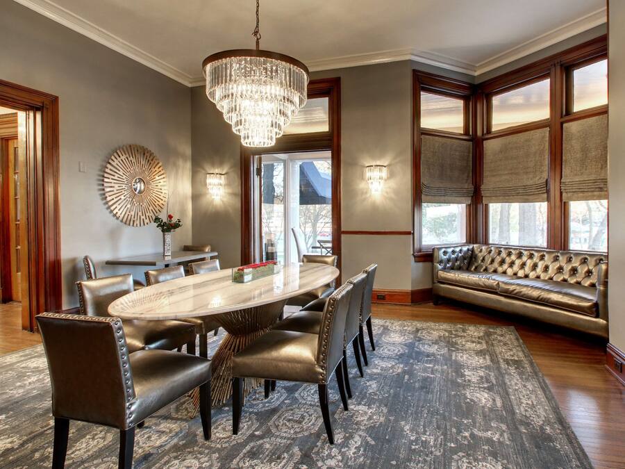 Un espace repas avec une grande table ovale, des chaises en cuir, un lustre et un tapis à motifs.