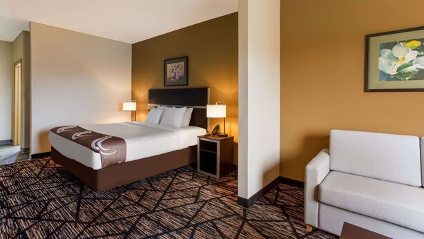 A hotel room with a bed, bedside lamps, a chair, and a framed picture on the wall. - Quality Inn & Suites Pearl - Jackson (Pearl)