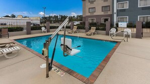 A swimming pool with lounge chairs and a lifeguard chair, surrounded by a fence and a building with multiple windows. - Quality Inn & Suites Pearl - Jackson (Pearl)
