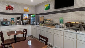 A hotel breakfast area with a microwave, coffee maker, and refrigerator. There are also tables and chairs for guests to sit and eat. - Quality Inn & Suites Pearl - Jackson (Pearl)