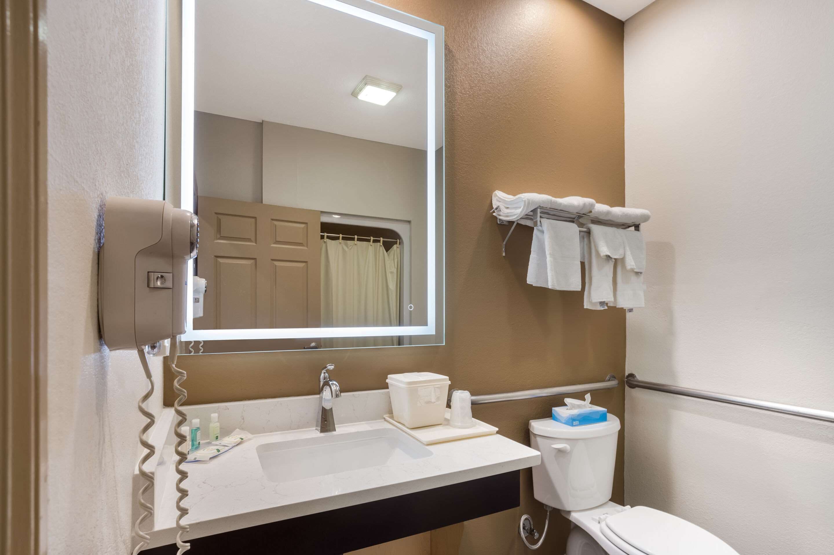 A bathroom with a sink, mirror, towel rack, toilet, and a hand dryer.