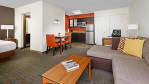 Habitación de hotel con cama, sofá, mesa de centro, escritorio con silla, kitchenette y baño.