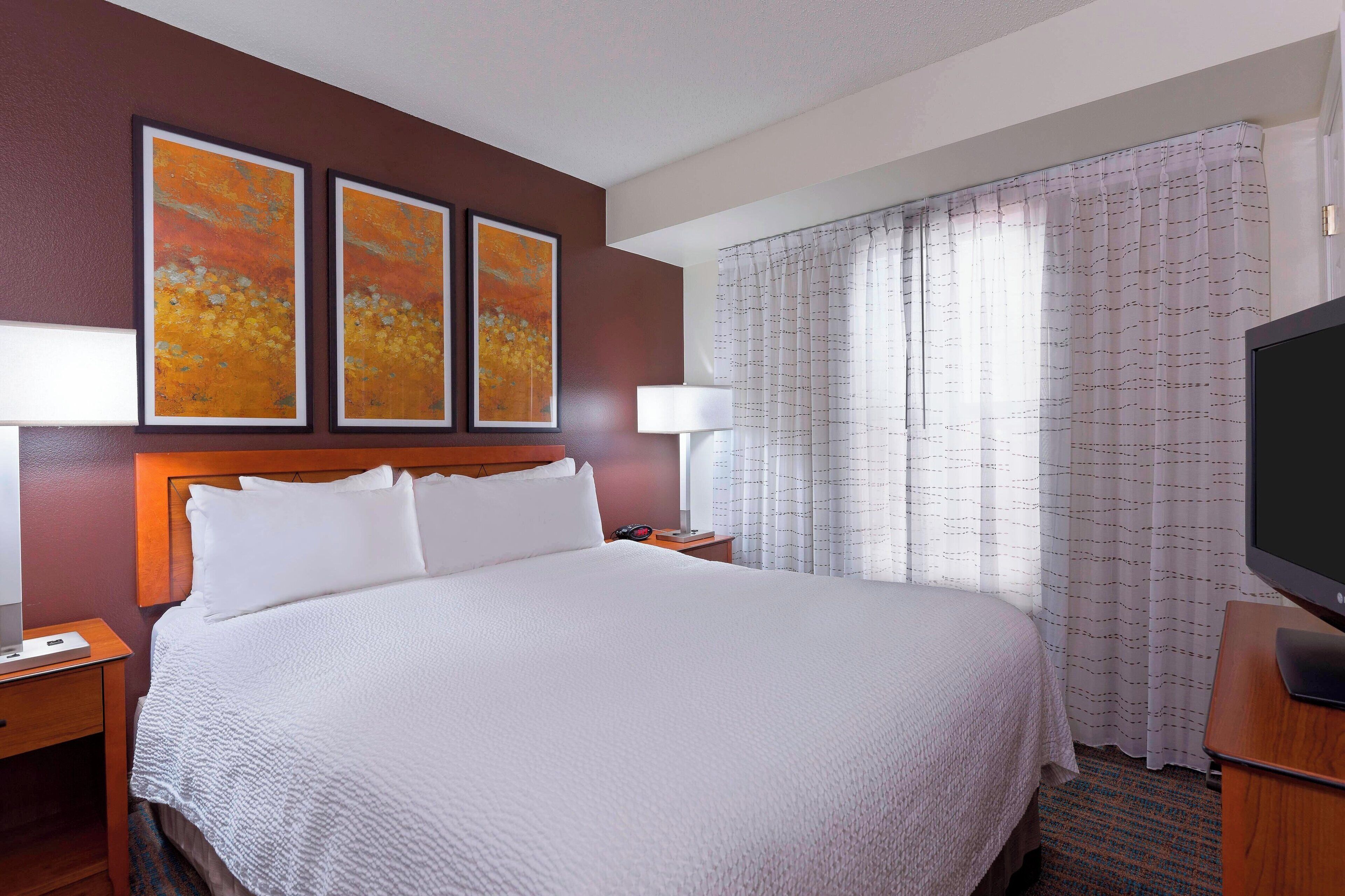 A hotel room with a large bed, two bedside tables, a TV, and two framed artworks on the wall.