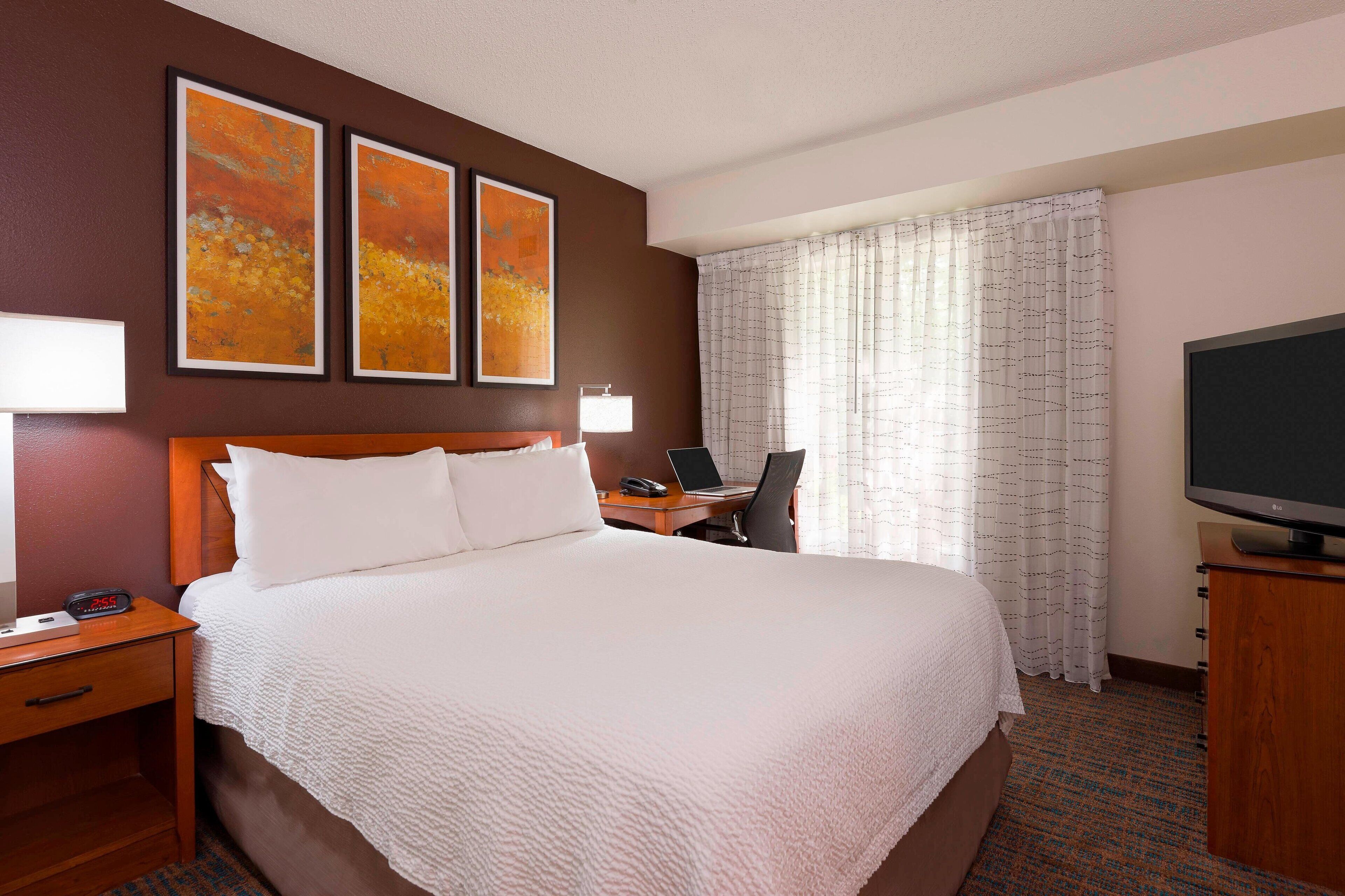 A hotel room with a large bed, a desk with a laptop, a television, and artwork on the wall.
