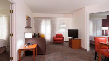 Una camera d'albergo con un letto, una scrivania, una TV, una poltrona rossa e un divano.