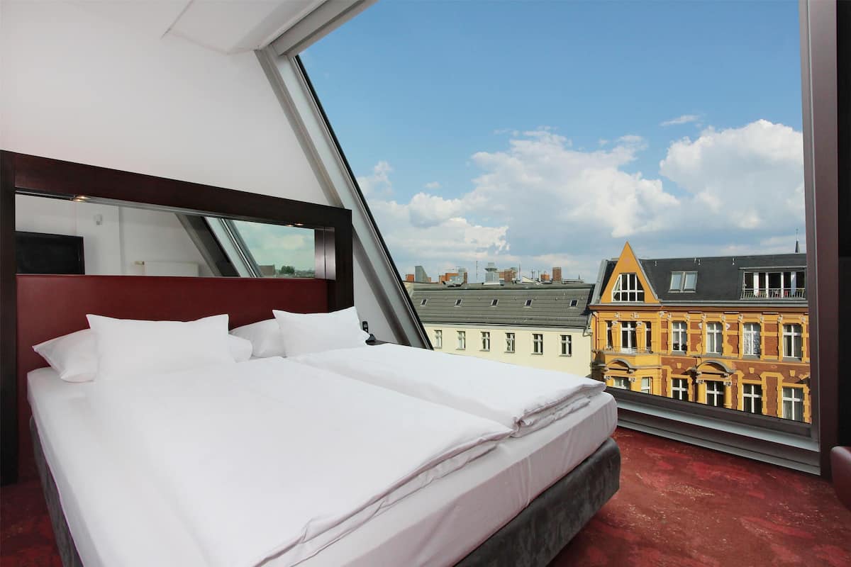 A hotel room with a bed, a large window, and a view of buildings.