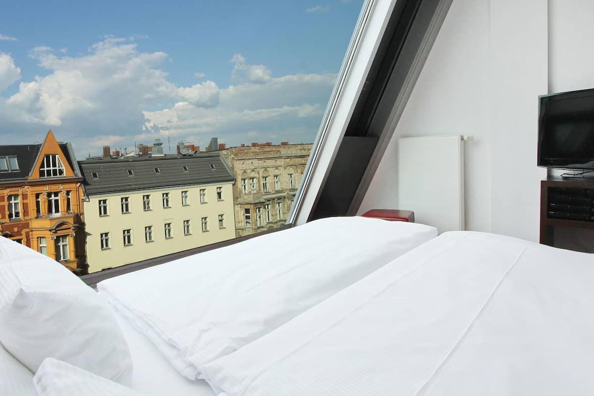 A hotel room with a bed, a television, and a view of historic buildings.