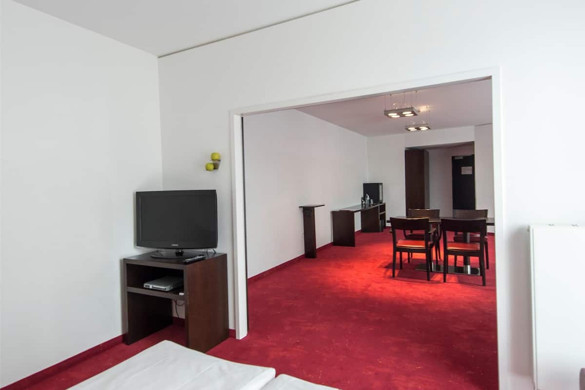 A hotel room with a bed, a TV, a desk, and a red carpeted hallway.