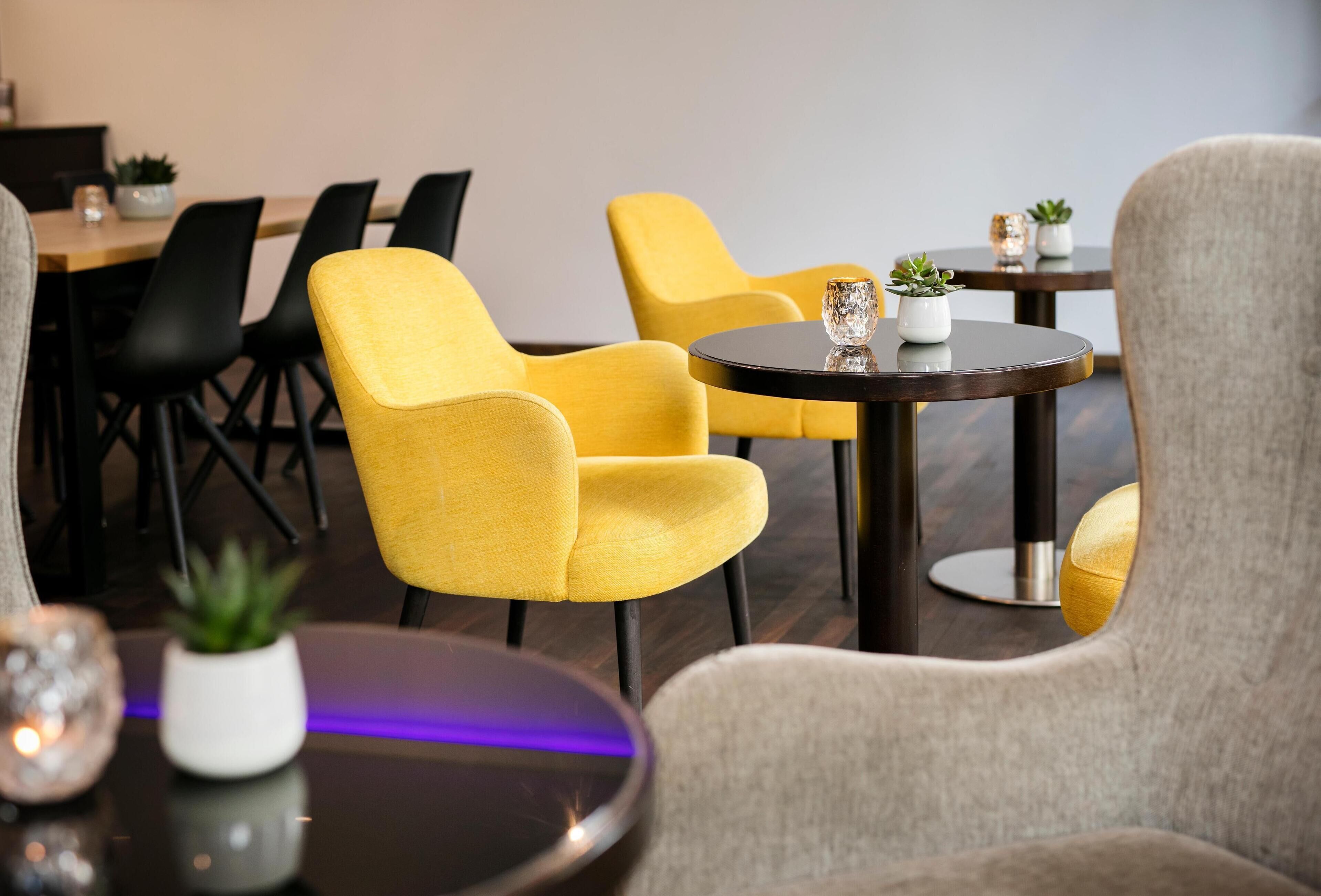 Ein modernes Interieur mit gelben Stühlen, einem runden Tisch und einem grauen Sessel.