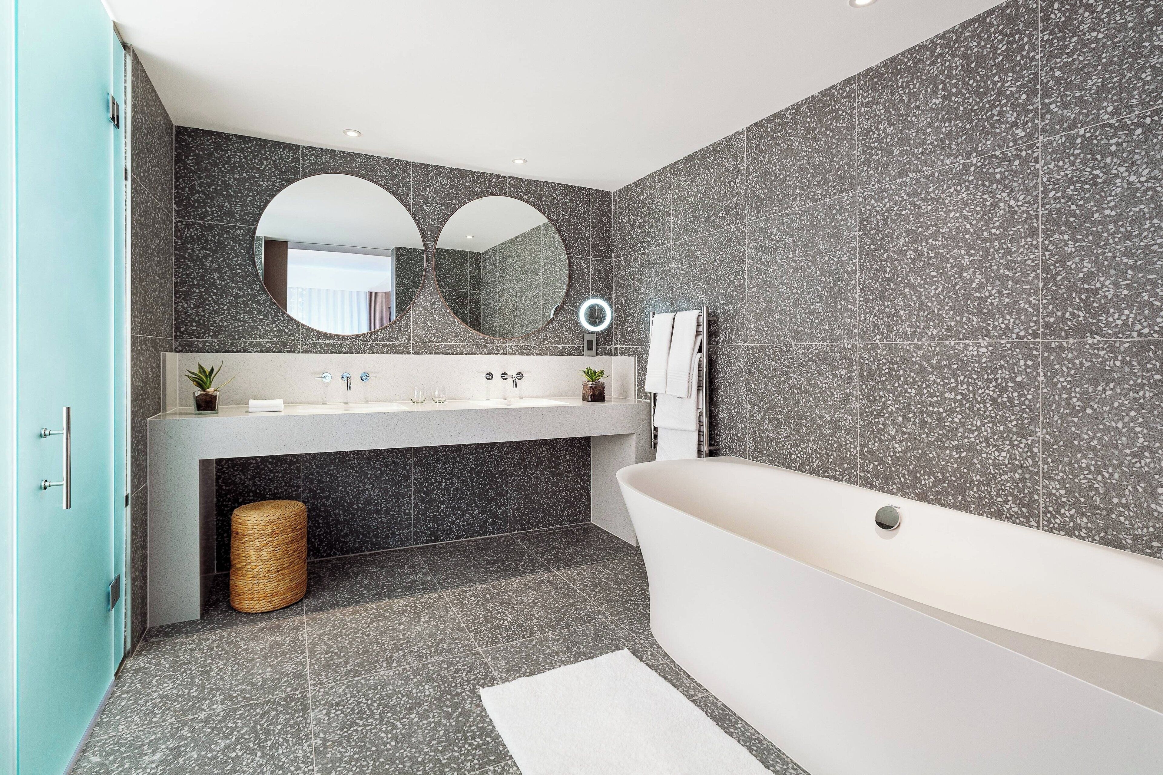 Ein modernes Badezimmer mit einer freistehenden Badewanne, einem Waschtisch mit Spiegel und einem runden Spiegel über dem Waschbecken.