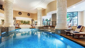 An indoor swimming pool with ornate columns, lounge chairs, and a view of the outdoors. - Malta Marriott Resort & Spa (St. Julian's)