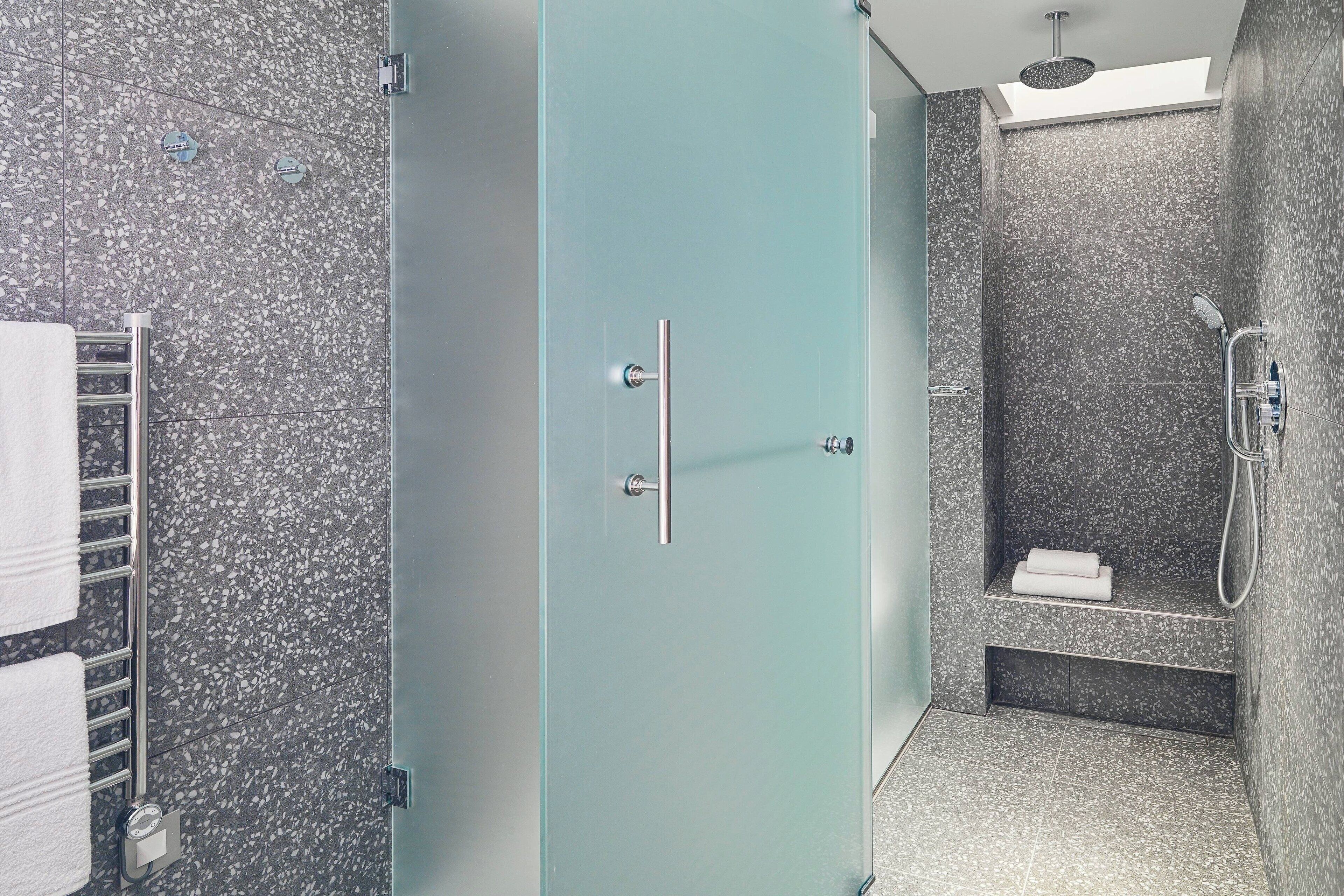 A modern bathroom with a glass door, a shower with a handheld showerhead, and a towel rack with towels.