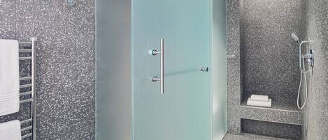 A modern bathroom with a glass door, a shower with a handheld showerhead, and a towel rack with towels.