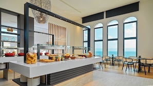 A modern breakfast bar with a variety of food items, large windows with a view of the sea, and a contemporary interior design.