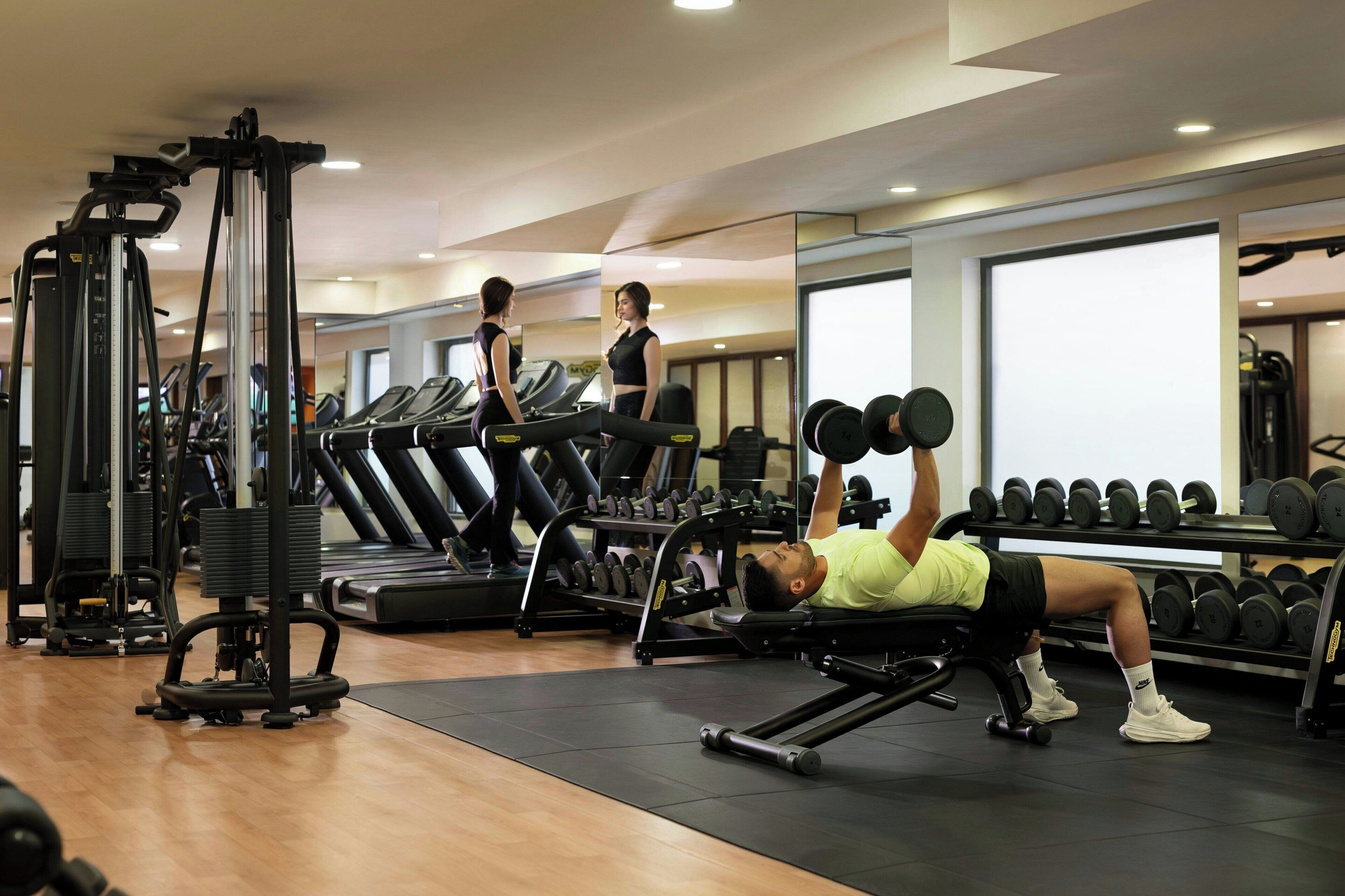 Academia com equipamentos de ginástica, esteiras e uma pessoa levantando pesos.