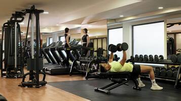 Academia com equipamentos de ginástica, esteiras e uma pessoa levantando pesos.