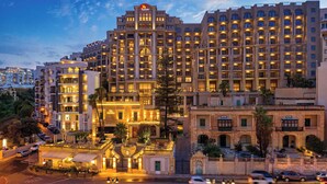 A large, multi-story hotel with a central atrium, multiple balconies, and a well-lit facade. - Malta Marriott Resort & Spa (St. Julian's)