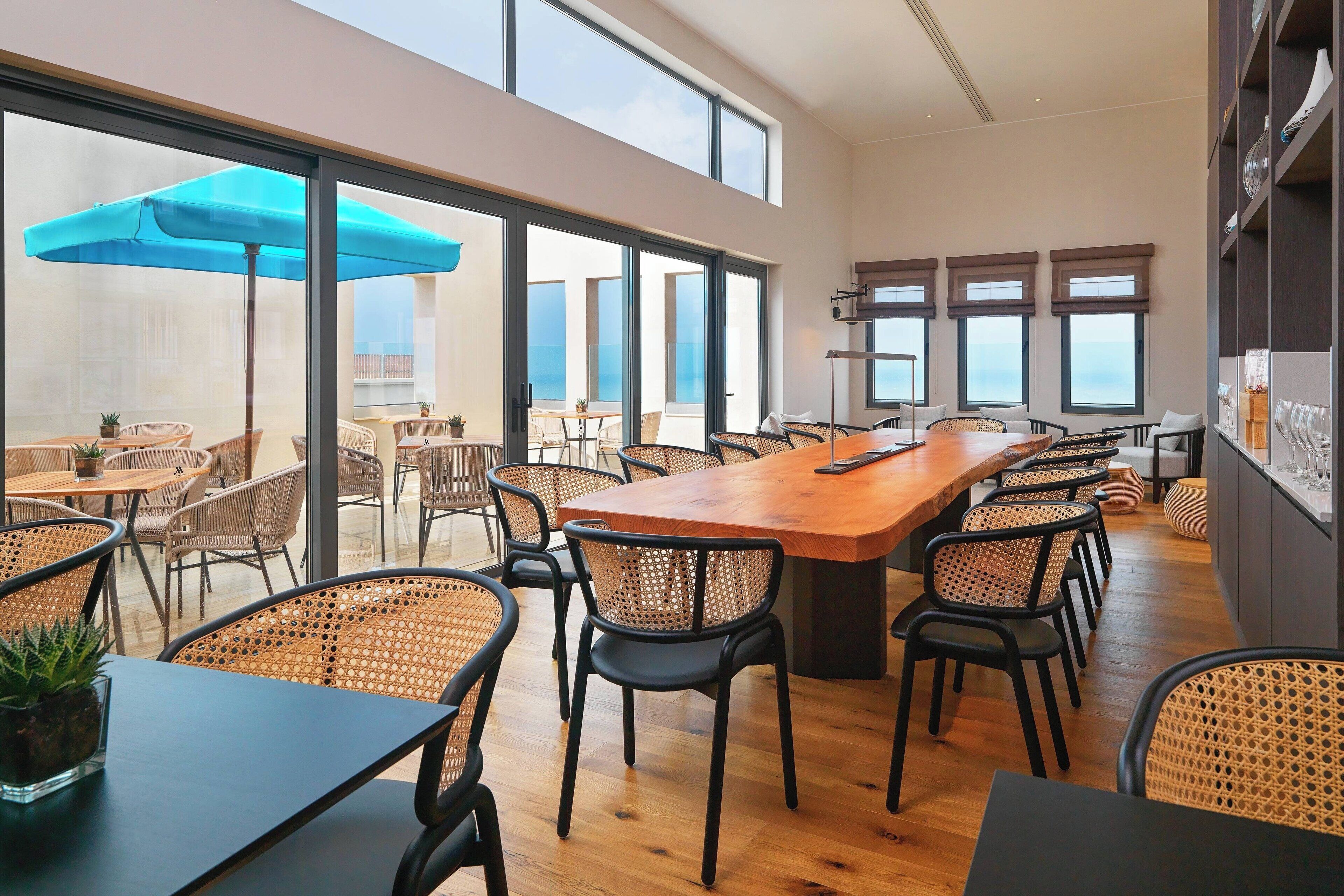 Un'ampia sala da pranzo con un lungo tavolo in legno e numerosi posti a sedere, grandi finestre che offrono vista sul mare e un'atmosfera luminosa e ariosa.