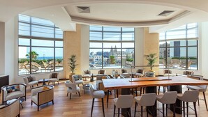 A spacious indoor area with large windows, a central wooden table, and multiple seating arrangements. - Malta Marriott Resort & Spa (St. Julian's)