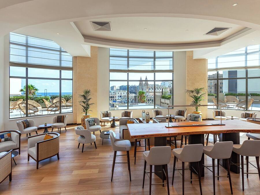 Un amplio espacio interior con ventanas grandes, una mesa de madera central y varios conjuntos de asientos.