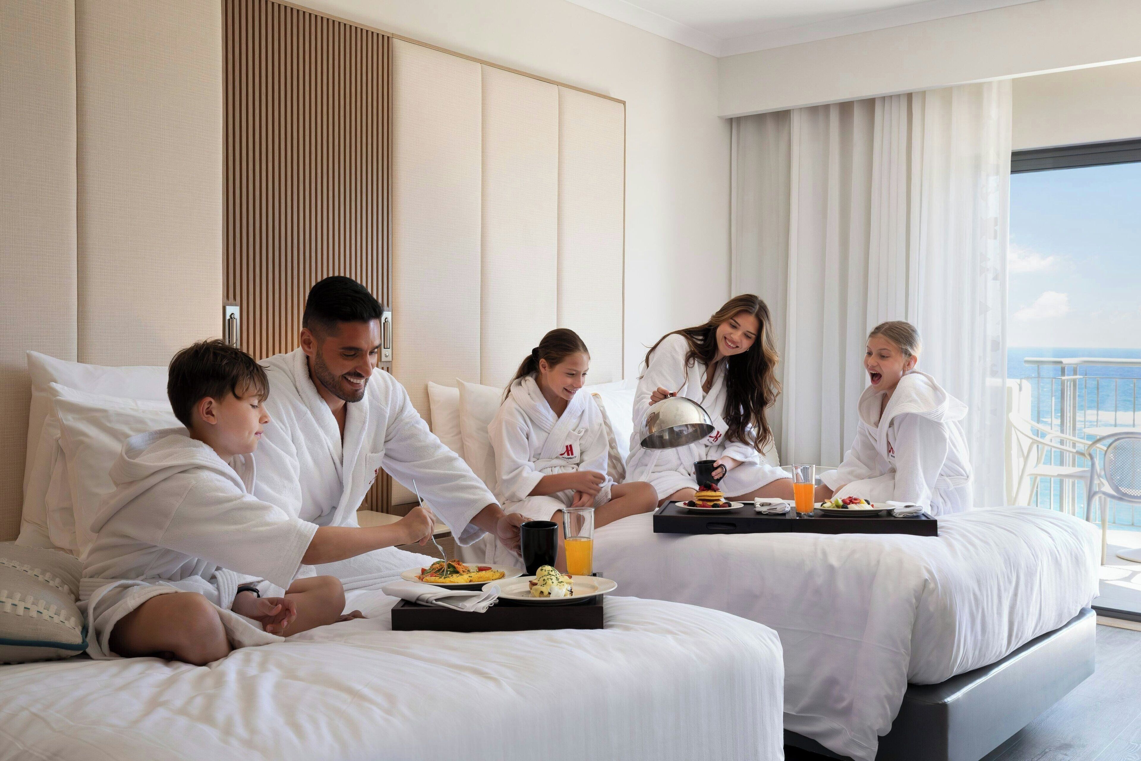 Habitación de hotel con cama, mesita de noche con artículos de desayuno y vista al mar.
