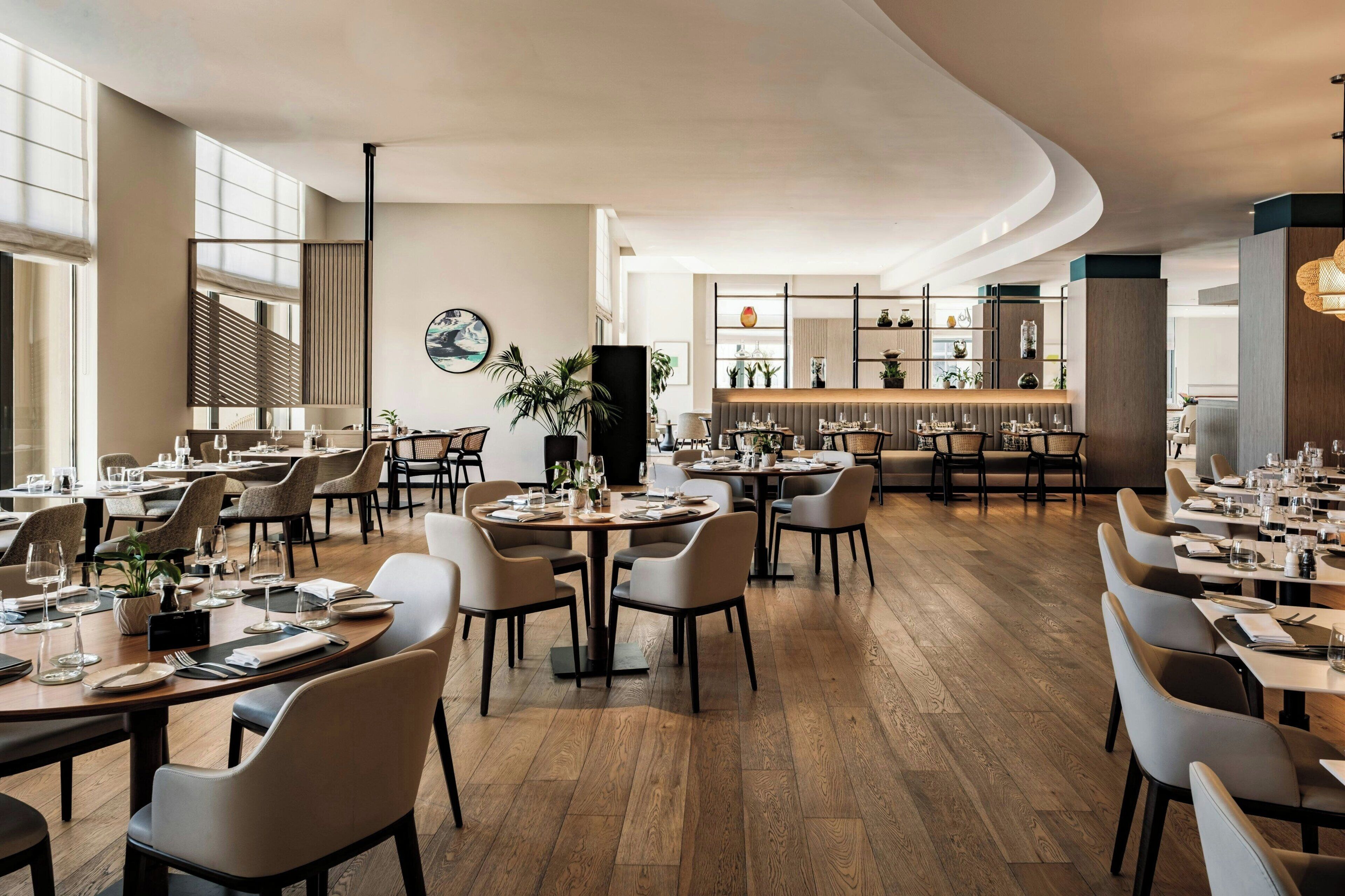 A modern restaurant with round tables, high ceilings, and a bar area.