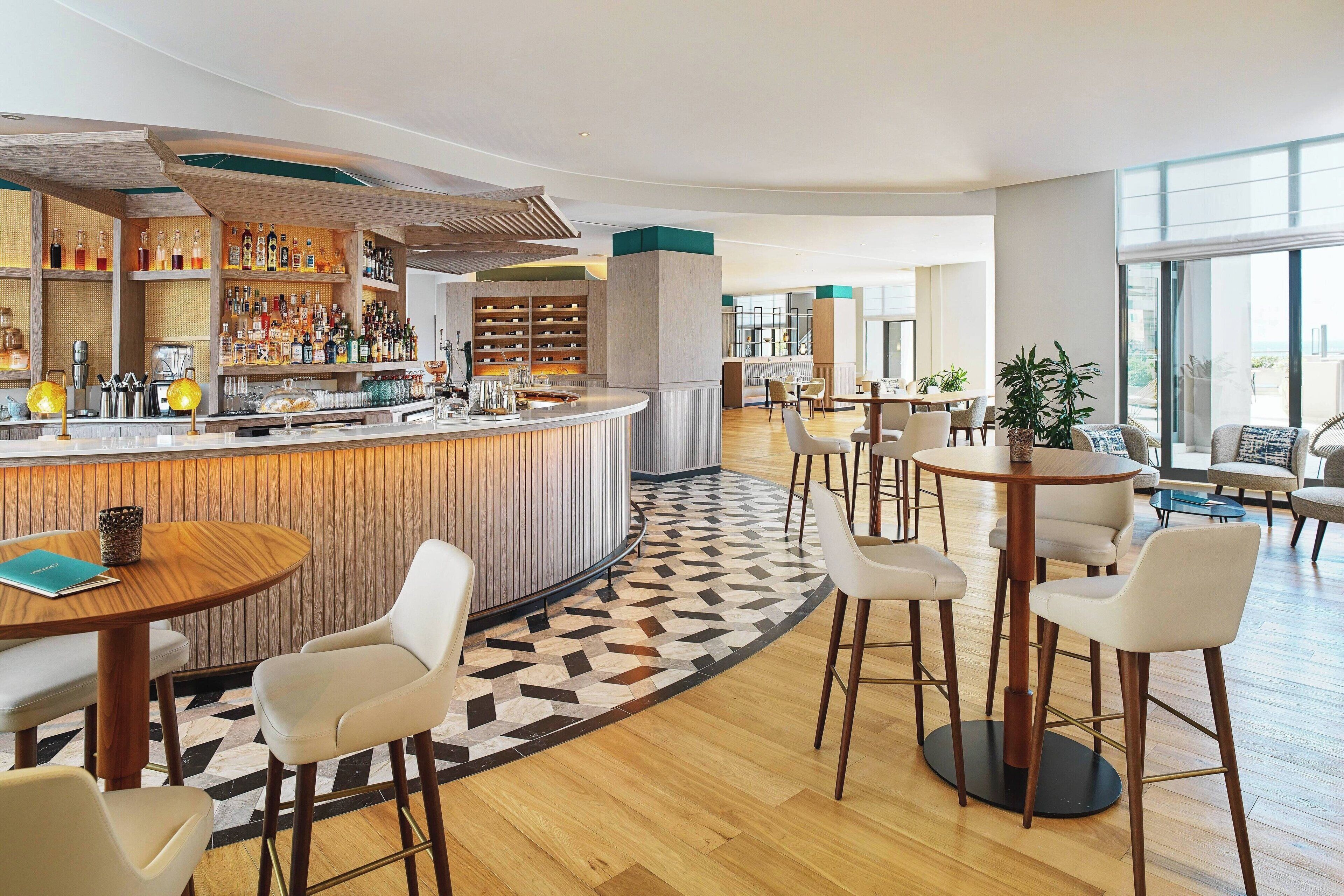 Un espace bar moderne avec un comptoir incurvé, des tabourets de bar blancs et un sol à motifs.