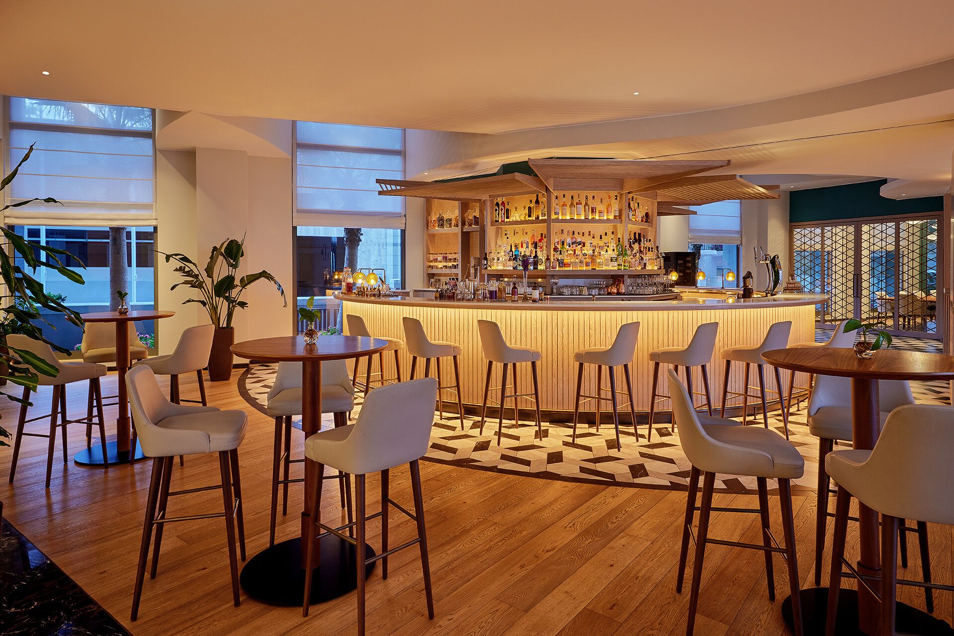 Un bar moderno con diversas opciones de asientos, una barra bien surtida y grandes ventanales que dejan entrar luz natural.