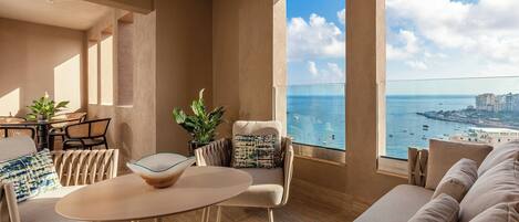 A modern living room with a large window overlooking the sea, a dining area with a table and chairs, and a sofa.