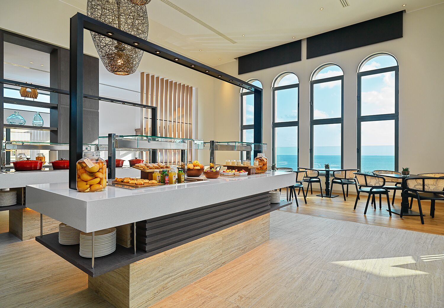 Een moderne ontbijtbar met uitzicht op zee, een buffet met diverse gerechten, en een zithoek met stoelen.