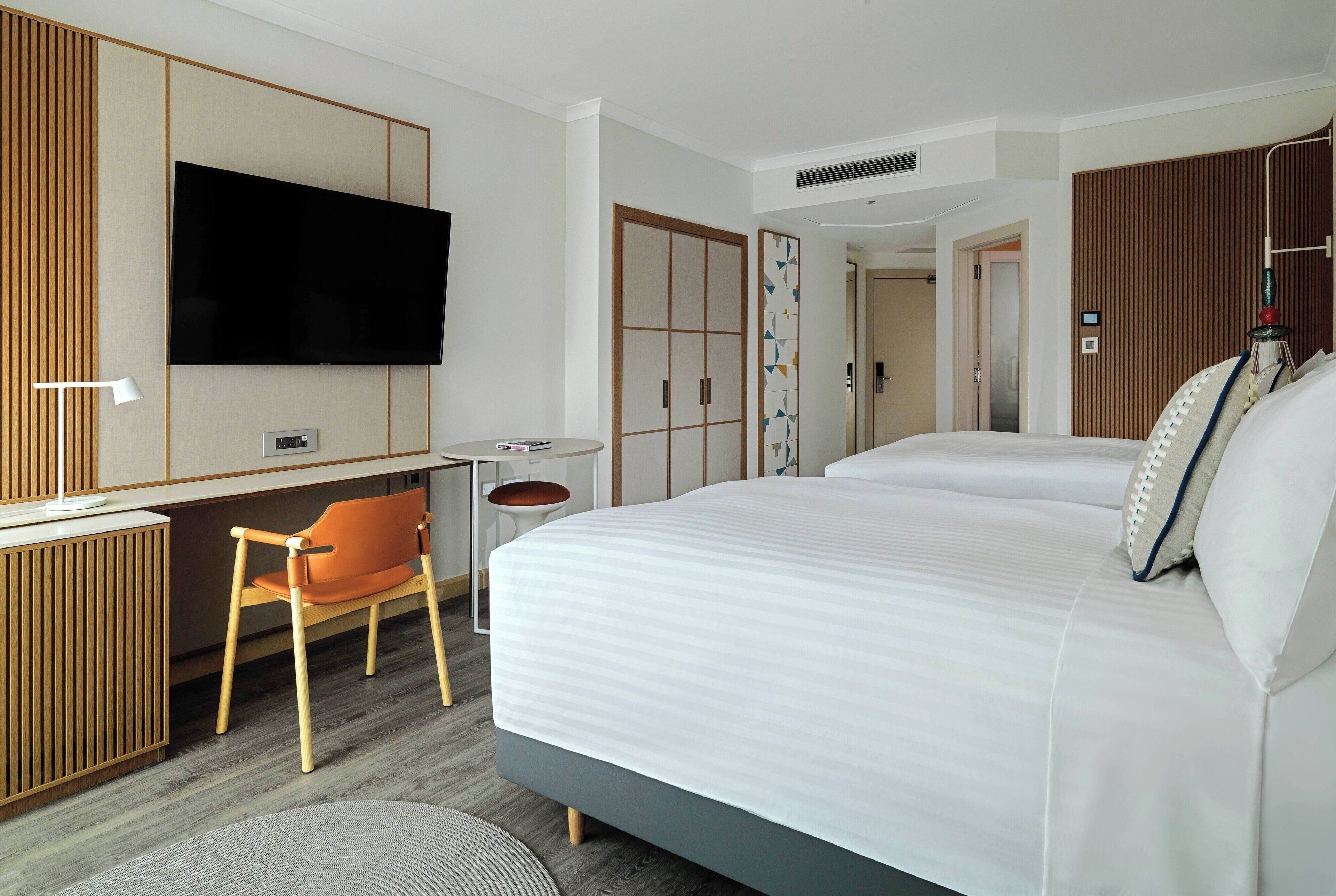 A hotel room with a large bed, a desk with a chair, a television, and a wardrobe.
