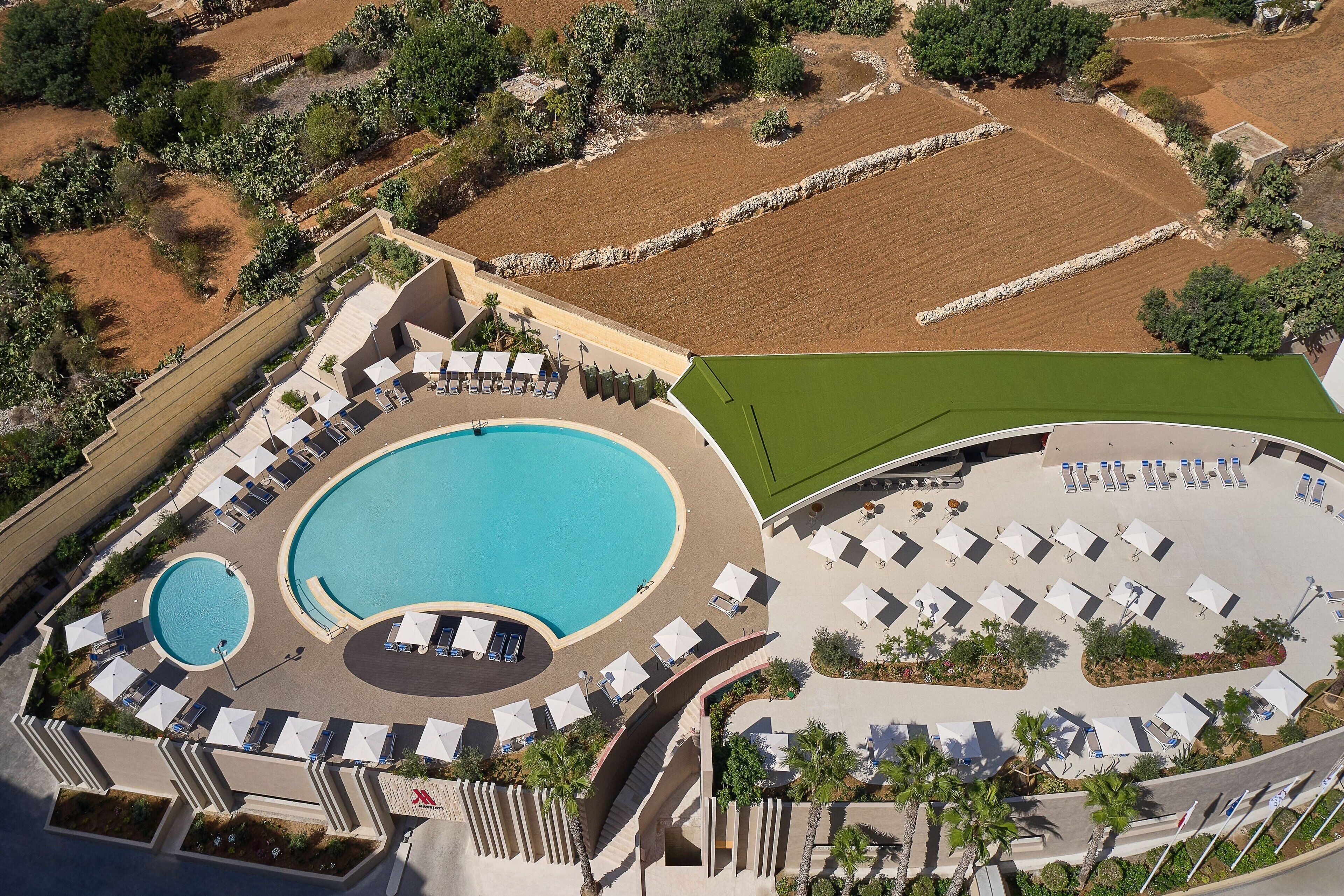 An aerial view of a resort with a large central pool, multiple sun loungers, and a well-maintained lawn area.
