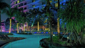 A hotel pool area with palm trees, lounge chairs, and a building with illuminated windows. - Le Méridien Kuala Lumpur (Kuala Lumpur)
