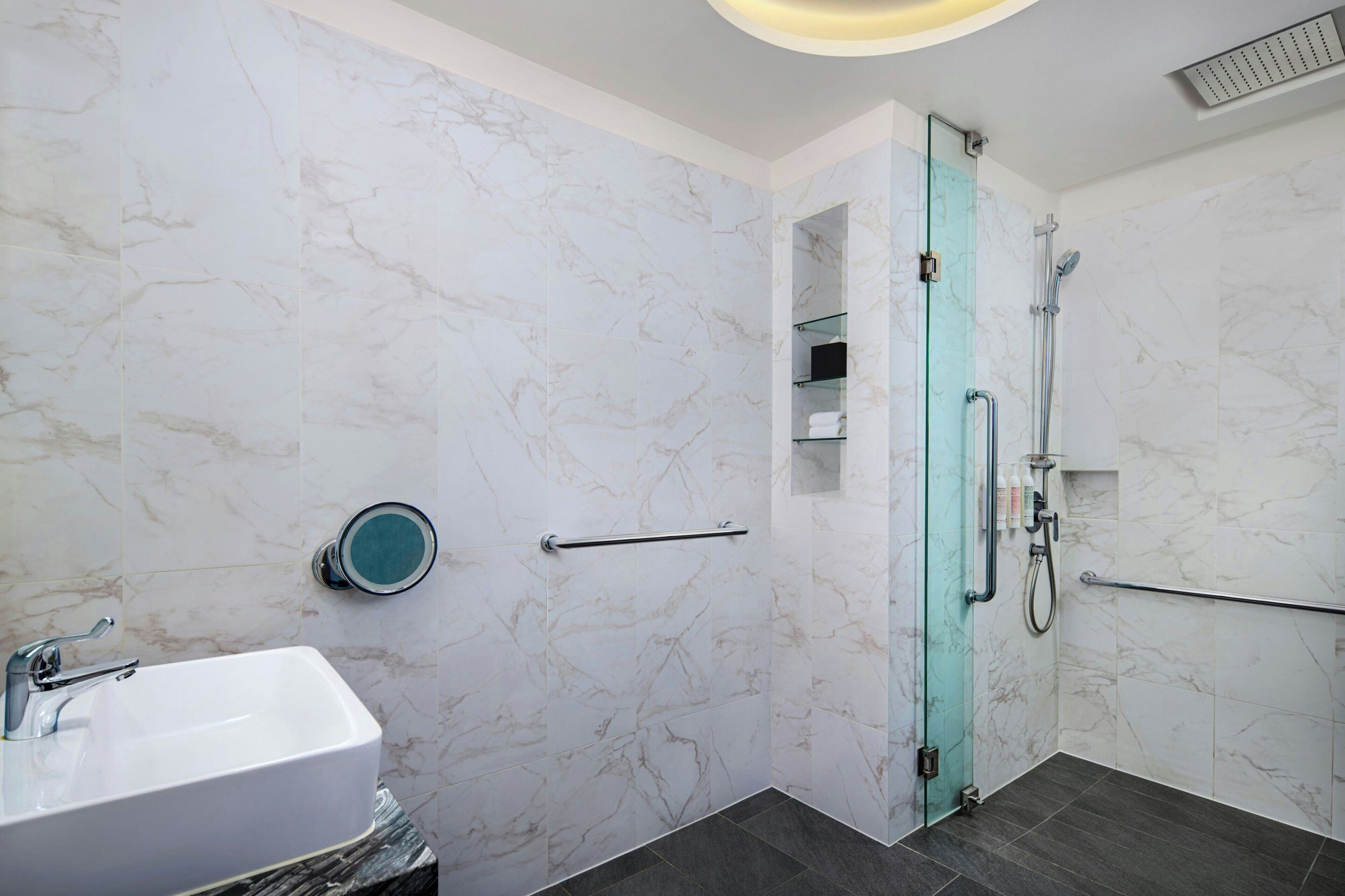 A bathroom with a white marble sink, a glass shower enclosure, and a marble-tiled wall.