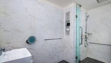 A bathroom with a white marble sink, a glass shower enclosure, and a marble-tiled wall.