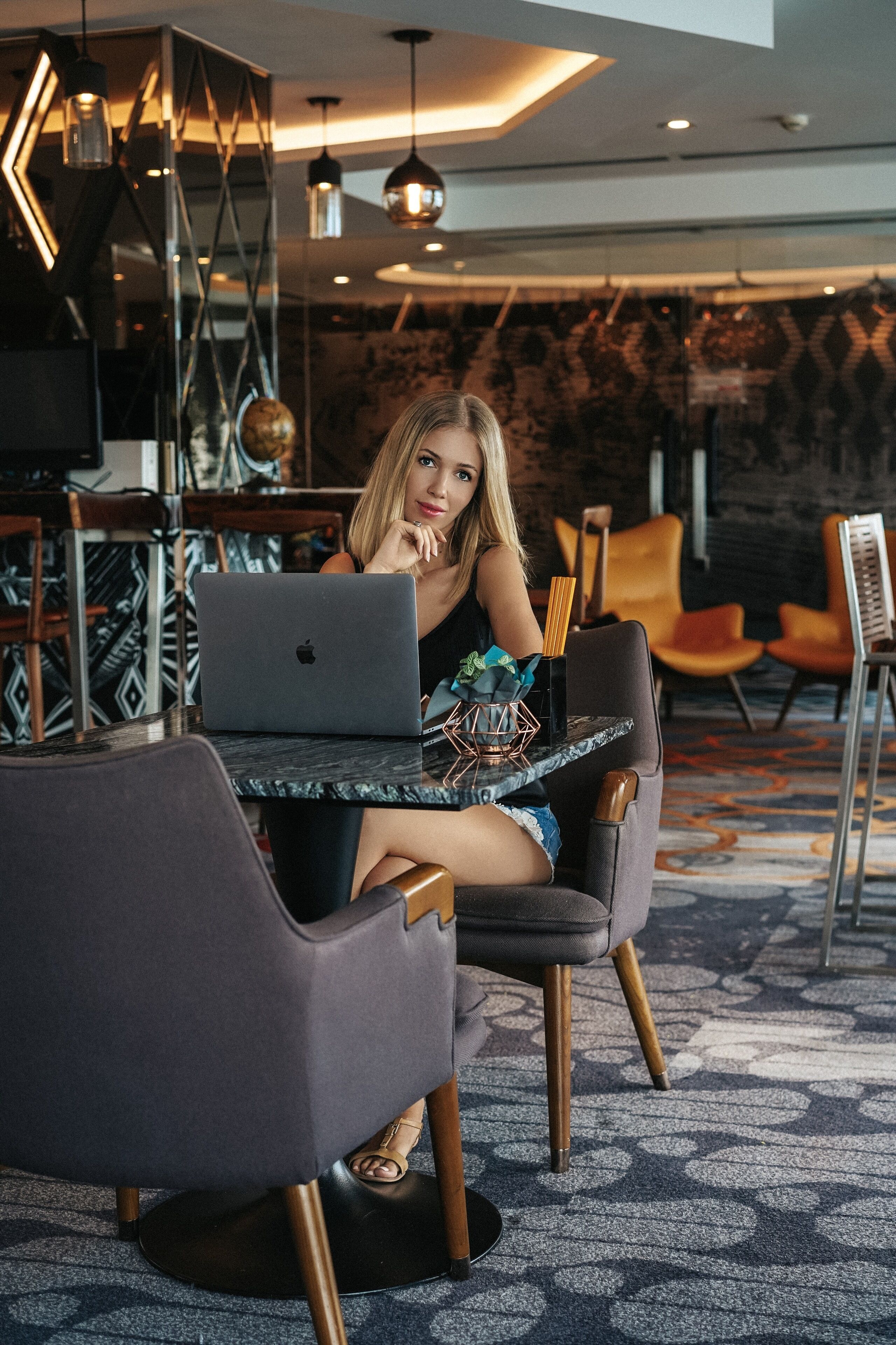 Un hall d’hôtel moderne avec un espace repas, comprenant une table sur laquelle se trouve un ordinateur portable, un globe terrestre et des meubles contemporains.