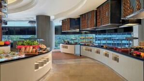 A modern hotel kitchen with a buffet setup, featuring a curved counter, various food stations, and decorative wall panels. - Le Méridien Kuala Lumpur (Kuala Lumpur)